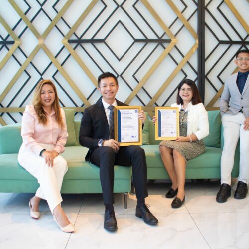 Karuna team members holding ISO 9001 and ISO 27001 certificates after achieving dual certification for ICT services.